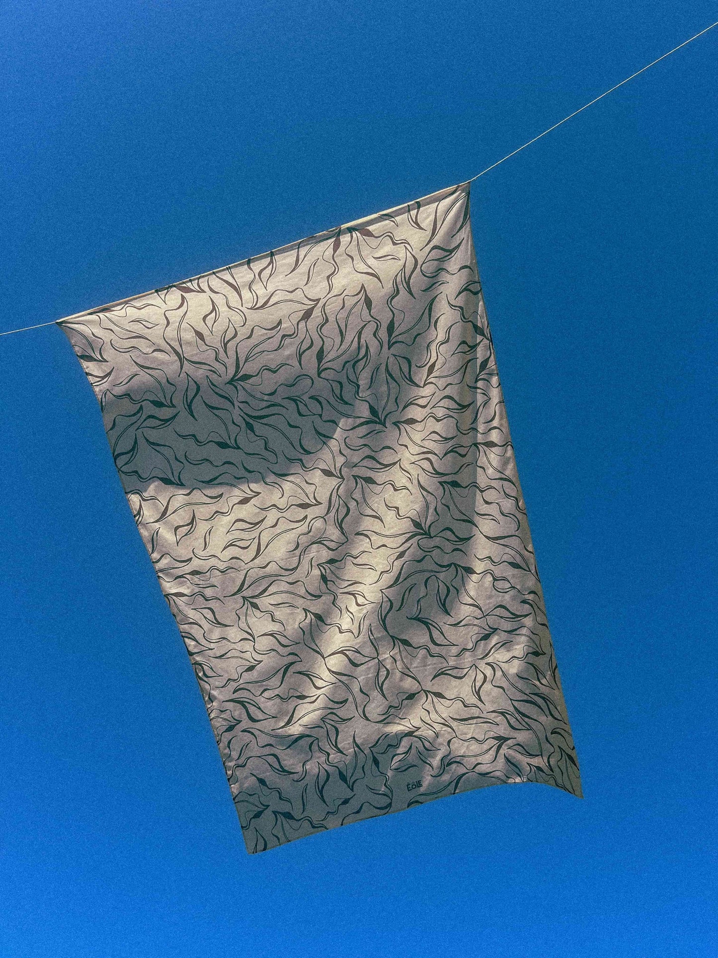 Paréo EOLE motif organique beige et brun flottant au vent sous un ciel bleu - 100% coton bio - Création éthique et artistique
